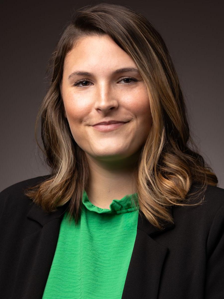 Ms. Gabriella Nanes, a Caucasian female, smiles at the camera wearing a green shirt with a black dress jacket.